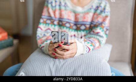 Glückliche junge Frau, die smartphoneÂ mobil sucht, verbringt Zeit vor dem Weihnachtsbaum zu Hause, um Neujahr und Chri zu feiern Stockfoto