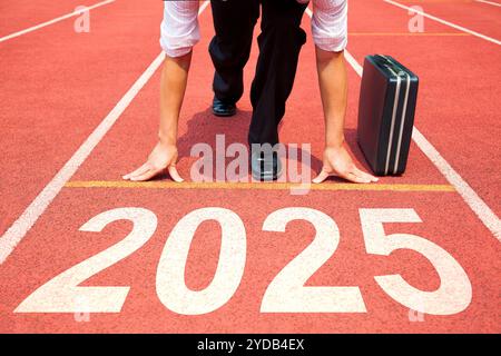 Happy New Year 2025 Konzept. Geschäftsmann, der sich auf die Leichtathletikbahn vorbereitet, die mit dem Jahr 2025 graviert ist. Vorbereitung auf das neue Jahr Stockfoto