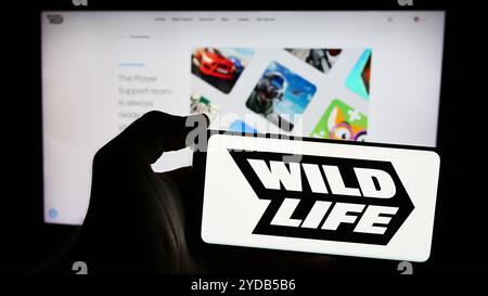 In dieser Abbildung hält eine Person ein Mobiltelefon mit dem Logo des brasilianischen Spieleunternehmens Wild Life Inc. (Wildlife Studios) vor der Webseite. Stockfoto