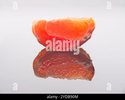 Grapefruitkeil auf weißer reflektierender Oberfläche. Stockfoto