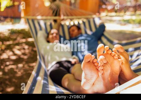 Ein junges verheiratetes Paar entspannt sich im Hinterhof des Hauses. Ein attraktiver Ehemann und eine Frau liegen draußen in einer Hängematte. Stockfoto