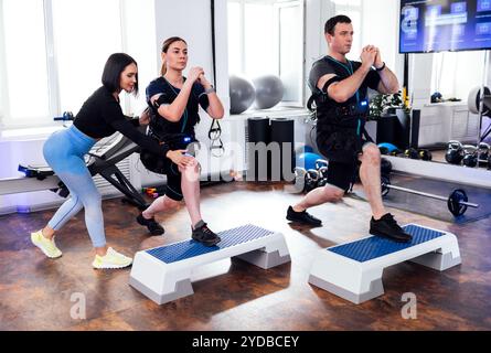 Ein junges Sportpaar in ems-Kostümen trainiert mit einem persönlichen Trainer im Fitnessclub. Mann und Frau mit geballten Händen, die mit Schritt nach vorne gehen Stockfoto