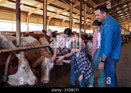 Eine glückliche Bauernfamilie in einem Kuhstall. Ein junges verheiratetes Paar und ihre Kinder kümmern sich um Haustiere auf dem Bauernhof. Stockfoto