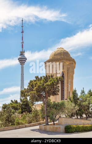 Das Denkmal der ewigen Flamme steht stolz inmitten üppiger Grünflächen, während der Fernsehturm von Baku unter einem klaren blauen Himmel in Baku, Aserbaidschan, im Hintergrund aufsteigt Stockfoto