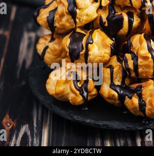 Profiterolen mit Schokoladencreme auf schwarzer Platte Stockfoto