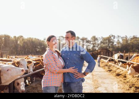 Eine junge Frau und ein Mann in lässiger Kleidung lachen und umarmen sich in einem offenen Kuhstall. Eine glückliche Familie von Bauern draußen. Ein AT Stockfoto
