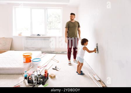 Renovierung des Apartments. Der kleine Junge hilft seinem Vater, an die Wände zu gehen. Ein junger Mann in legeren Klamotten mit süßem Sohn repariert im Zimmer. Vater und Kind A Stockfoto