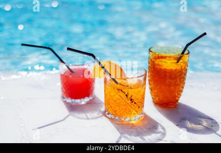 Nahaufnahme von drei Gläsern mit köstlichen kühlen Cocktails am Pool. Tassen mit leckeren frischen Fruchtsäften auf blauem Hintergrund Stockfoto