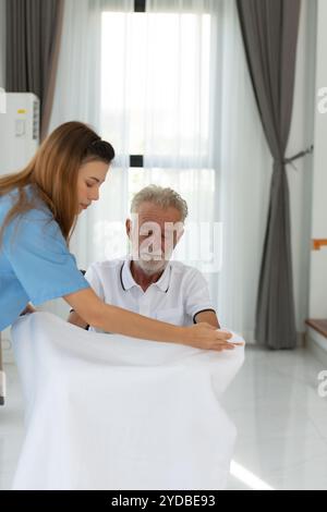 Der Arzt zieht eine Decke auf, um sich aufzuwärmen und spricht mit einem älteren Patienten mit Depression. Im Wohnzimmer des Hauses Stockfoto