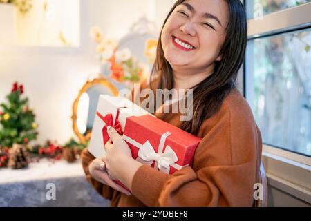 Glückliche asiatische Frau, die Geschenkbox umarmt. Empfang eines Weihnachtsgeschenks. Fröhliches Mädchen mit Weihnachtsgeschenk oder offenem Weihnachtsgeschenk boxÂ Neujahrsgeburt Stockfoto