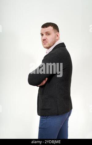 Seitenansicht des eleganten jungen Geschäftsmannes, der mit Armen über grauem Hintergrund steht Stockfoto