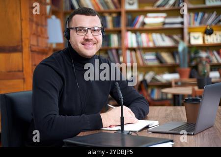 Männerblogger streamen von der Bibliothek mit Laptop und Mikrofon Stockfoto