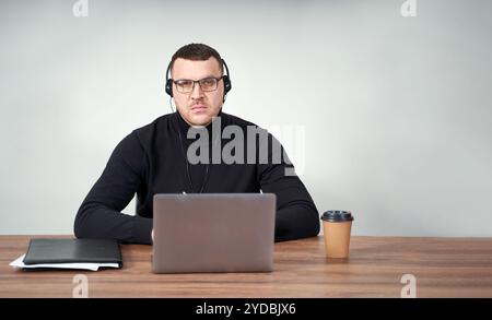 Konzentrierter Mann in Kopfhörern mit Laptop, während er über grauem Hintergrund mit Hintergrund sitzt Stockfoto