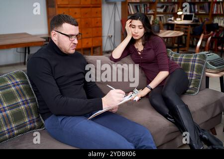 Weibliche Patientin, die mit ihrem Therapeuten spricht, der sich Notizen im Privatbüro macht Stockfoto