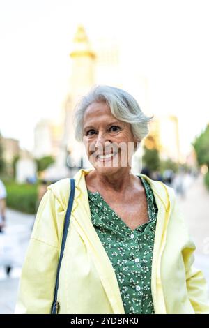 Vertikales Nahporträt einer glücklichen älteren modernen Frau, die in der Stadt steht und in die Kamera lächelt Stockfoto