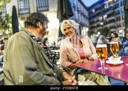 Ältere männliche und weibliche Freunde unterhalten sich beim Bier in der Stadt und sitzen auf der Bürgersteig-Bar Stockfoto