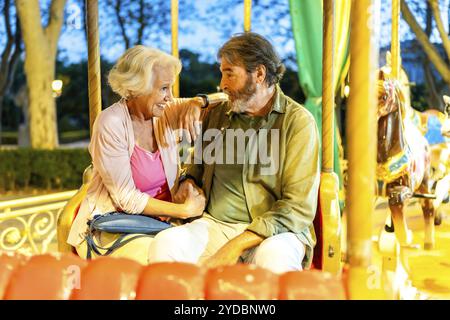 Modernes Seniorenpaar, das nachts in einem bunten Karussell zusammen sitzt Stockfoto