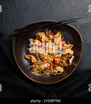 Nudeln mit Gemüse und Huhn in einer schwarzen Schüssel anbraten Stockfoto