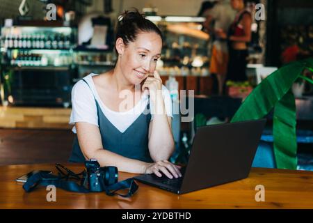 Zufriedene, glückliche Fotografin, die in einem Café an einem Laptop arbeitet. Stockfoto