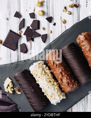 Französische Dessert-Eclairs oder Profiterolen mit verschiedenen Schokoladenglasur auf einem schwarzen Steinteller Stockfoto