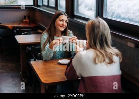 Lächelnde Brünette, die mit einer Freundin in einem Café plaudert. Stockfoto