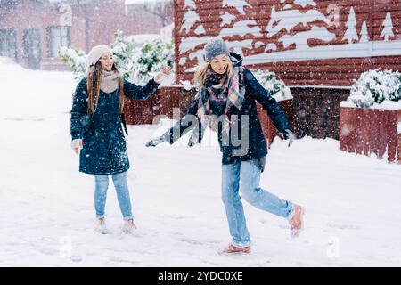 Zwei junge Frauen spielen Schneebälle und lachen beim Spaziergang durch eine verschneite Stadt Stockfoto