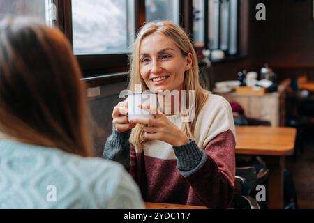 Porträt einer attraktiven Blondine, die mit einem Freund plaudert, während sie in einem gemütlichen, warmen Café sitzt. Stockfoto