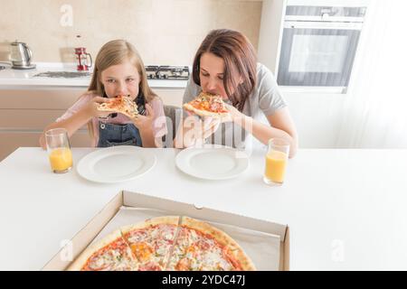 Mutter und Tochter in der Küche sitzen, essen Pizza und Spaß haben. Fokus auf Tochter Stockfoto