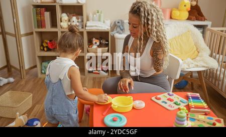 Mutter und Tochter spielen in einem farbenfrohen Spielzimmer voller Spielzeuge, die Wärme und Liebe ausstrahlen, während sie kreative Aktivitäten ausführen und die Familie symbolisieren Stockfoto