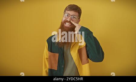 Hübscher rothaariger bärtiger Mann, der selbstbewusst vor gelbem Hintergrund posiert und seine Nase mit einem Finger berührt. Stockfoto