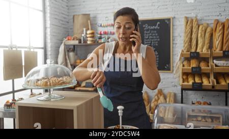 Frau sprach am Telefon, während sie in einer Bäckerei mit leckerem Brot und Gebäck arbeitete Stockfoto