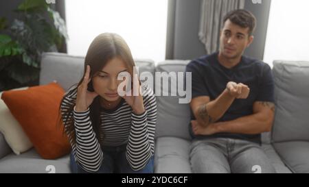 Frau, die gestresst aussieht, während der Mann während eines Gesprächs auf einem Sofa in einem modernen Wohnzimmer Gesten macht, was auf Beziehungsspannungen hindeutet Stockfoto