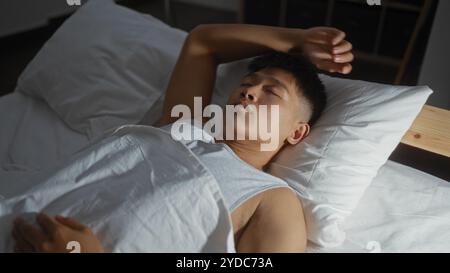 Junger Mann, der in einem Schlafzimmer mit weißen Laken und Kissen schläft, unterstreicht eine friedliche Inneneinrichtung und eine komfortable Wohnumgebung. Stockfoto