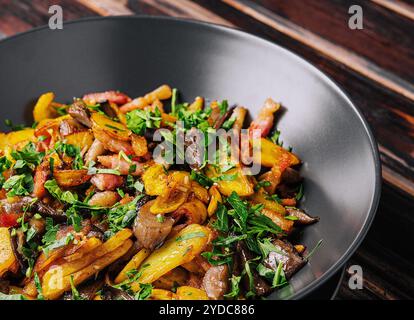 Gebratene Kartoffeln mit Pilzen auf einem schwarzen Teller Stockfoto