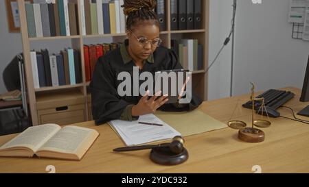 Frau in einem Richterbüro, die Dokumente auf einem Tablet überprüft, umgeben von Rechtsbüchern, Justizmaßstäben und einem Hammer, der einen professionellen Rechtsberater zeigt Stockfoto