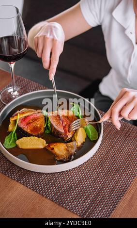 Weibliche Hände halten Gabel und Messer und schneiden Ente mit Wein Stockfoto