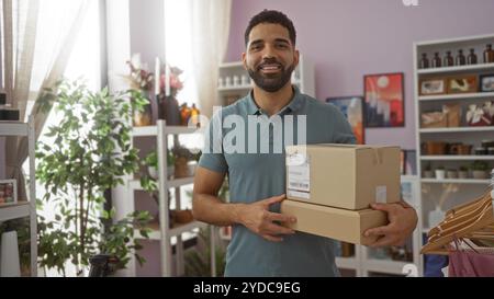 Der junge Mann hält Pakete in einem gut dekorierten Haus-Dekorationsgeschäft mit Pflanzen und Regalen, die mit verschiedenen dekorativen Artikeln gefüllt sind. Stockfoto