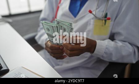 Eine afroamerikanische Ärztin in einer Klinik, die us-Dollar-Scheine an ihrem Arbeitsplatz zählt. Stockfoto