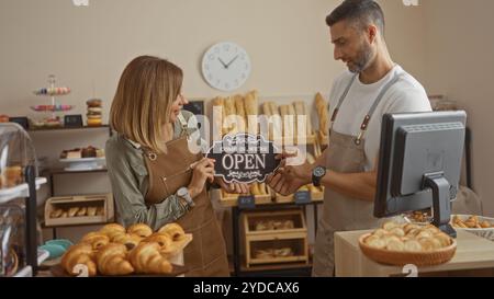 Männer und Frauen, die ein offenes Schild im Inneren der Bäckerei mit Backwaren halten Stockfoto