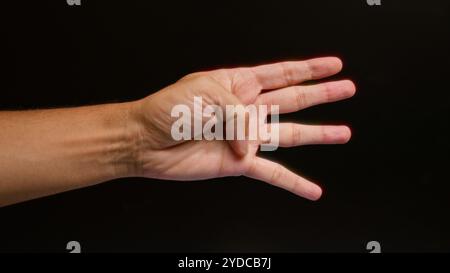 Die Hand des Mannes vor dunklem Hintergrund zeigt eine Geste mit vier gestreckten Fingern. Stockfoto