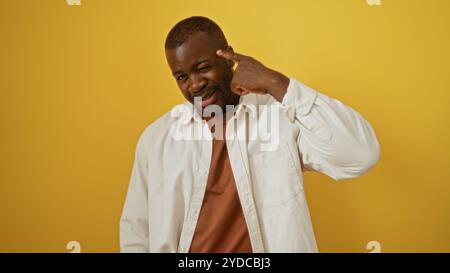 Ein junger afroamerikanischer Mann gibt spielerisch Gesten vor einem lebhaften gelben Hintergrund und hebt eine selbstbewusste und attraktive Persönlichkeit hervor. Stockfoto