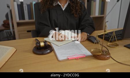 Hispanische Richterin arbeitet in einem Büro, schreibt Notizen mit Hammer und juristische Dokumente auf dem Schreibtisch Stockfoto