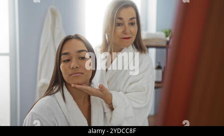 Mutter und Tochter in weißen Bademänteln genießen eine gute gemeinsame Zeit in einem Spa-Ambiente, das sich in einem Spiegel mit beruhigendem Wellness-Innenraum spiegelt Stockfoto