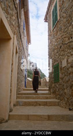 Frau, die durch eine enge Steinstraße in Port de valldemossa mallorca spanien zwischen rustikalen Gebäuden unter bewölktem Himmel läuft Stockfoto