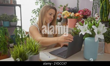 Eine junge Frau arbeitet an einem Laptop, umgeben von leuchtenden Blumen in einem gemütlichen Blumenladen. Stockfoto