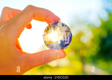 Die Hand hält ein kugelförmiges Puzzleteil, das in hellem Licht getaucht ist und Teamarbeit und Zusammenarbeit auf internationaler Ebene symbolisiert. Stockfoto