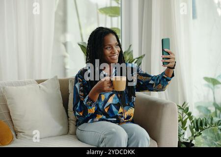 Lächelnde Frau, Die Selfie Nimmt, Während Sie Einen Kaffeetasse Hält Stockfoto
