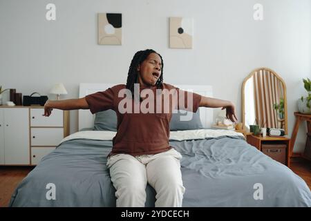 Gähnende Frau, die auf Bett im Schlafzimmer sitzt Stockfoto