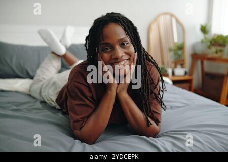 Lächelnde Frau, die sich auf dem Bett mit den Händen im Gesicht entspannt Stockfoto