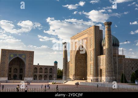 Samarkand, Usbekistan - 5. Juli 2024: Portal und Säulen in Ulug Beg und Sher-Dor Madrassa in der Registan von Samarkand mit Blumengarten bei Sonnenuntergang Stockfoto